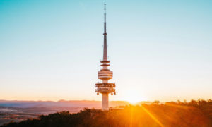 The sun is setting behind a tower on top of a hill